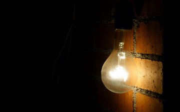 включенная лампочка на кирпичной стене в тёмной комнате - минимализм